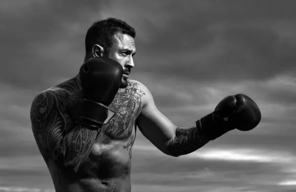 Sport boxing. Sportsman boxer fighting on sky background. Strong athletic man with boxing gloves punching. Boxer punch