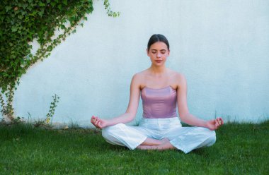 Bahar Parkı 'nda meditasyon yapan yoga kadını. Kadın esniyor. Genç kız yoga yapıyor, egzersiz yapıyor, yeşil çimlerde çalışıyor.
