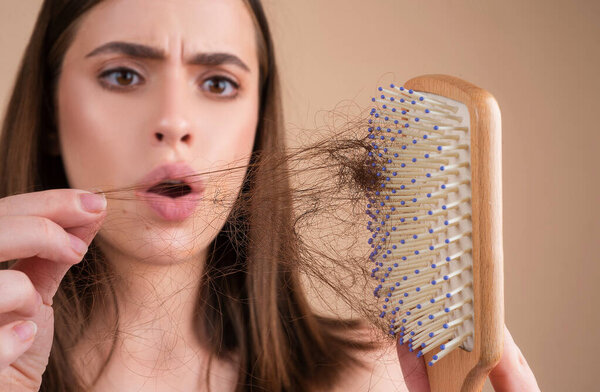 Выпадение волос. Женщина расстроена потерей волос. Портрет грустной девушки с проблемными волосами, изолированной. Беспокойная девушка с длинными поврежденными нездоровыми волосами в руке