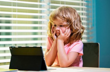 İnternetteki çocuk, evde eğitim görmüş. Küçük çocuk uzaktan öğretmenle çevrimiçi ders konuşması yapıyor, bilgisayarını kullanıyor, kapalı alanda ders çalışıyor.