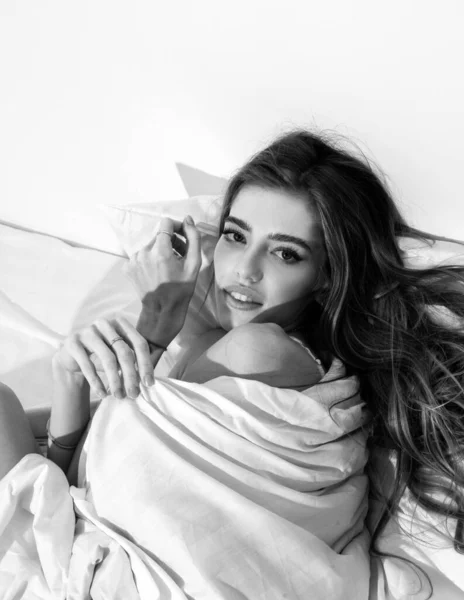 Sexy woman in the morning after good sleep in white comfortable bed, sensual girl lying on soft pillow in bedroom, morning relaxation concept