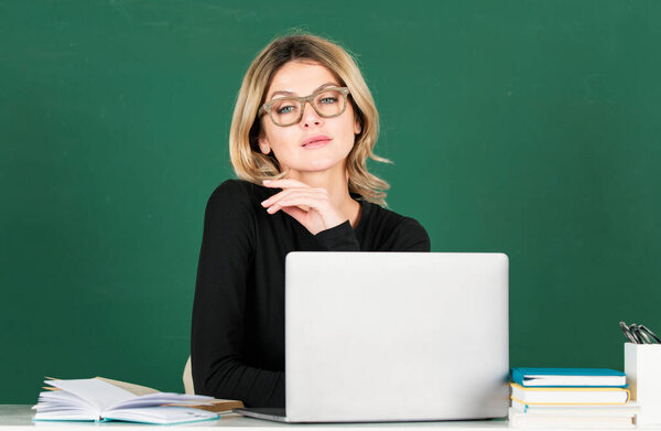 Portrait of teacher or female tutor working at table in school. Young women student studying in class