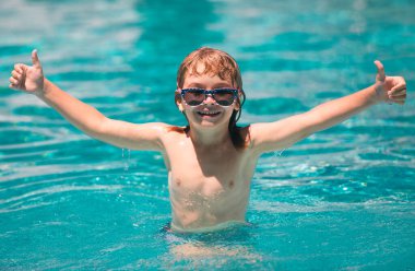 Çocuk yüzme havuzunda yüzüyor. Güneş gözlüklü heyecanlı çocuk yaz günü havuzda