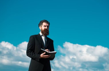 Kendine güveni tam bir iş adamı, elinde not defteri ve kalemle gökyüzü arka planında