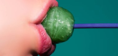 Ağzında lolipop var, yakın plan. Ağzında lolipop olan güzel bir kız. Parlak kırmızı kadın dudakları. Ağız yalamak chupa chup emmek