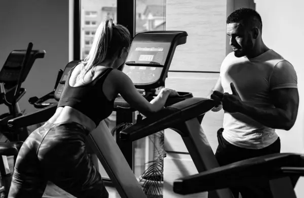 Sporty couple workout cardio exercise gym. Sportive couple in gym. Personal trainer fitness instructor helping woman doing cardio workout running
