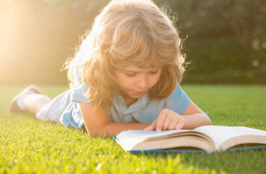 Dışarıda kitap okuyan sevimli bir çocuk. Çocuk parkta kitap okudu.