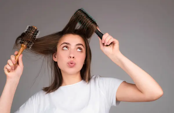 Funny woman combs her healthy hair. Combing healthy long straight female hair, close up. Attractive gorgeous cheerful positive girl combing shine silky hair, isolated