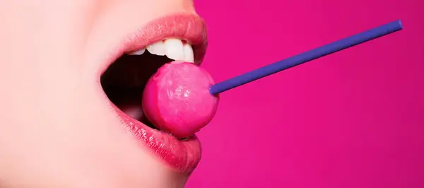 Licking candy. Lollipop model. Woman lips sucking a candy. Glamor sensual model with red lips eat sweats lolly pop isolated on pink