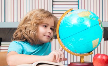 School kid pupil looking at globe in library at the elementary school. World globe. School kid 7-8 years old with book go back to school. Little student. Education concept