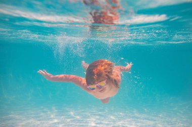 Çocuk yaz havuzunda su altında yüzer. Yaz çocukları tatil konsepti. Komik çocuklar yüzlerini suyun altına çevirir. Yüzme havuzunda su sıçratan çocuk. Yaz sporu. Çocukla yaz tatili