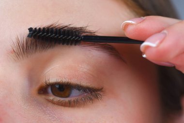 Kaşlar şekilli. Kadının kaş makyajı yaptırmasına yakın çekim. Makro kaşına fırçayla kozmetik uyguluyordu. Mükemmel bir kaş şekli, kahverengi göz farı ve uzun kirpikleri. Şekli kaşlar