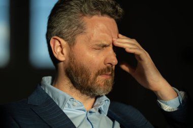 Baş ağrısı çeken yorgun bir adam. Başa dokunmak, ağrıyı dindirmek, migren. İş sorunları. İflas, mali sorun ve kriz konsepti. Bin yıllık İspanyol adamın başı ağrıyor. Migren.