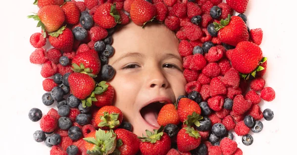 The kids face with fruit and berries. Summer strawberry, blueberry, raspberry, blackberry background. Top view photo of child face in berries background. Healthy kids eating