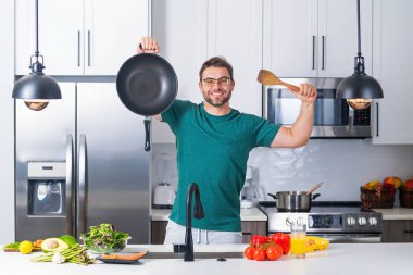 Mutfakta yemek yapan adam. Yakışıklı adam Modepn mutfağında lezzetli yemekler hazırlıyor. Erkek aşçı mutfakta yemek pişiriyor. Milenyum adamı mutfağın arka planında sağlıklı bir yemek hazırlıyor. Mutfak aletleri