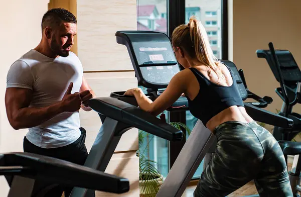 Sporty couple workout cardio exercise gym. Sportive couple in gym. Personal trainer fitness instructor helping woman doing cardio workout running