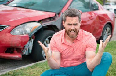 Stresli sürücü yolda kırık arabanın yanında oturuyor.