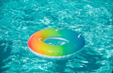 Inflatable ring floating in pool on summer background. Rainbow swimming pool ring float in blue water. Concept color summer