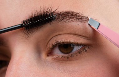 Kaş makyajı. Makro, kaşlarını kapat. Kaşlarını yakından fırçalayan bir kadın. Mikro patinaj, modelleme kaşları