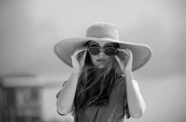 Close-up portrait of young woman by the sea. Girl in sunglasses and straw hat standing at the seaside