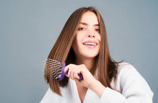 Woman combing hair. Portrait of female model with a comb brushing hair. Girl with hairbrush. Close up female face