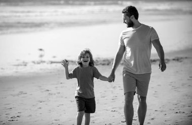 Baba ve oğul yaz plajında yürüyor. Baba ve çocuk el ele tutuşup birlikte yürüyorlar. Aile seyahati, tatil, babalar günü konsepti