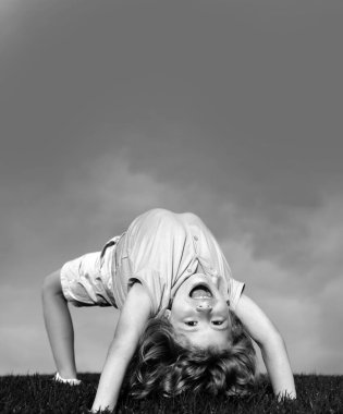 Yeşil çimlerin üzerinde baş aşağı duran mutlu çocuk. Gülen çocuk bahar parkında eğleniyor. Sağlıklı çocuk yaşam tarzı konsepti. Spor çocuğu egzersiz yapıyor. İfade ifadesi