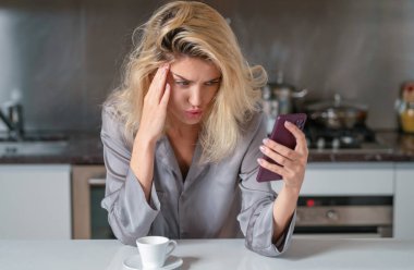 Sabah mutfakta bunalımlı bir kadın. Üzgün kadın sabah kahve içer ve evde telefon kullanır. Mutfakta seksi pijamayla akıllı telefonlardan konuşan mutsuz kadın.