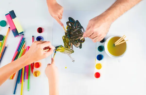 Desk of an artist hands with drawing painting colorful paints and pencil crayons on white background. Kids learning painting