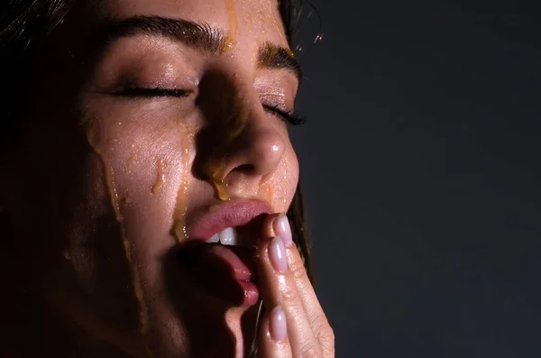 Fashion and beauty. Sensual young woman face with honey drop close up. Sexy model with honey drip on face