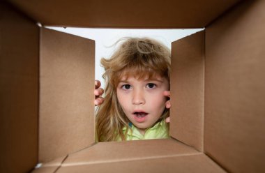 Çocuk paketleri açıyor ve karton kutuyu açıyor. Sürpriz bir suratla içeri bakıyor. Çocuk açma paketi