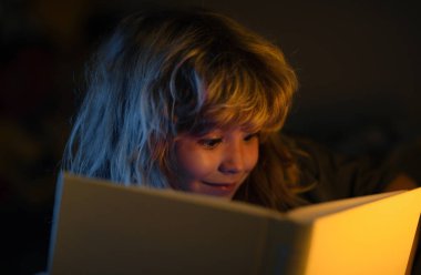 Çocuk uyumadan önce yatakta kitap okuyor. Evdeki küçük çocuk yatakta uzanıp kitap okuyor. Çocuğun gelişimi. Akıllı çocuk.