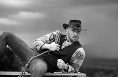 Çiftlikteki kovboy. Kovboy şapkalı ve antika kıyafetli yakışıklı bir adam. Arka planda kement ipi olan kovboy.