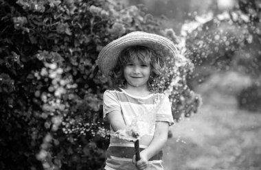 Hasır şapkalı şirin çocuk hortumla gülüyor.