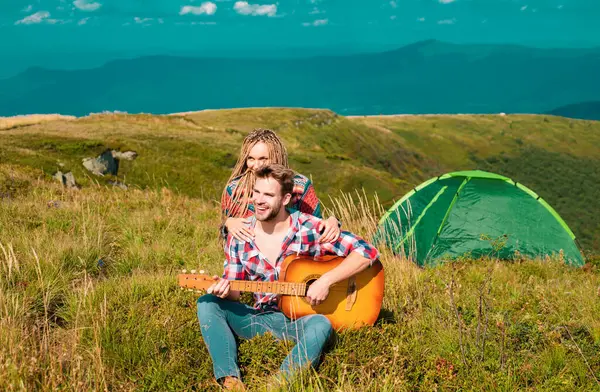 Romantic couple camping on spring landscape. Adventure for young lovers campers on nature, man with guitar