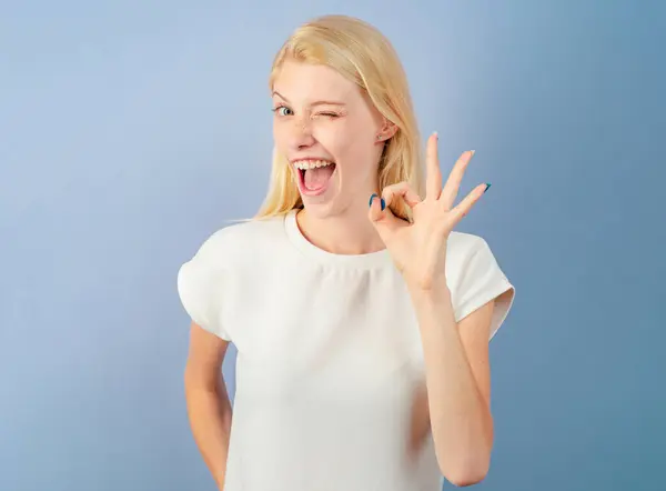 Laughing woman showing OK gesture. Woman isolated on white background showing ok sign with fingers. Funny young girl showing OK. Woman emotions. Emotional face