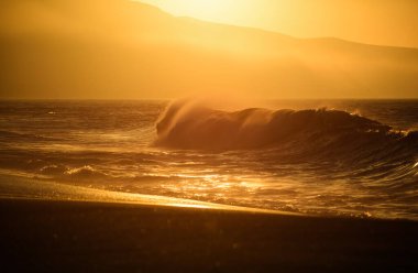 Altın gökyüzü ve deniz suyu. Tropikal denizin üzerinde sahil gündoğumu. Sahilde dalgaların sıçradığı renkli bir gün batımı. Dalgalar sıçrıyor