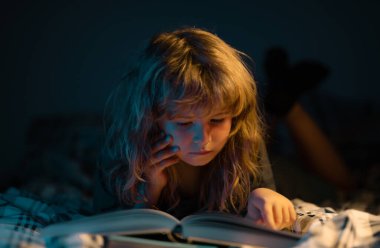 Yatakta uzanmış kitap okuyan sevimli bir çocuk. Çocuk yatmadan önce kitap okuyor. Çocukların hayal gücünün gelişimi.