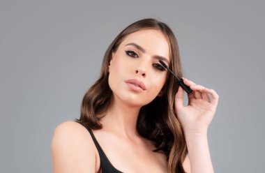 Kaş makyajı. Kaşlarını yakından fırçalayan bir kadın. Gri stüdyo arka planında izole kadın portresi