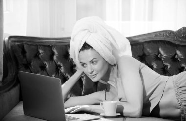 Evde pijama ve havlu giyen, dizüstü bilgisayar kullanan, kahve içen çekici bir genç kız.