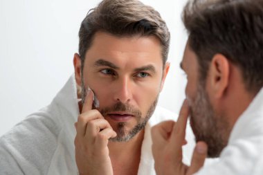 Yüz kremi süren İspanyol bir adamın güzel portresi. Cilt kremi, cilt yaşlanma önleyici kırışıklık etkisi. Adam cildine nemlendirici krem sürüyor. Cilt bakımı, erkek yüzü için kozmetik krem tedavisi