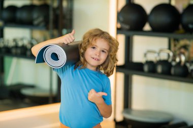 Spor salonunda yoga minderi tutan zinde bir çocuk. Yoga çocuk konsepti. Güçlü atletik fitness çocuğu. Çocuk Spor Konsepti