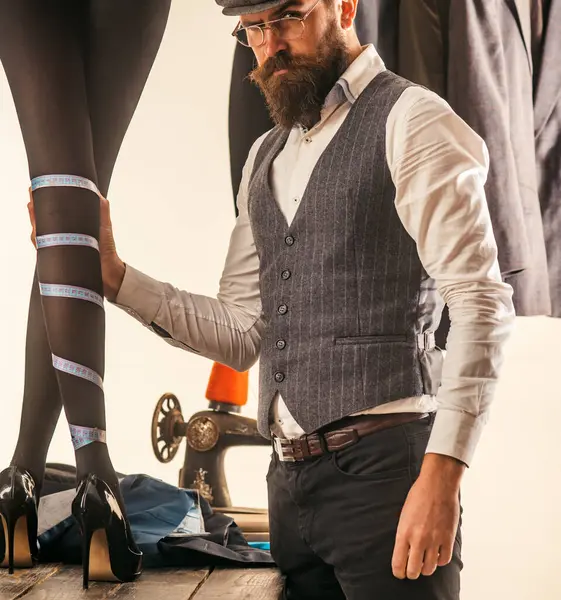 男装制造商 暗淡的概念 留胡子的老式服装制造商测量女性性感的长腿 缝纫车间里的女裁缝裁缝女裁缝男人为女人缝衣服 — 图库照片