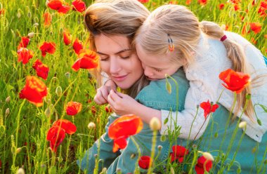 Çiçekli bir gelincik tarlasında yürüyen anne ve kızın portresi. Yaz aile tatilleri doğada. Gelincik çiçekli haşhaş çayırında yaz. Anne ve kızı baharda