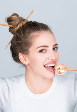 Yemek çubuklarıyla Japon suşisi yiyen güzel bir kız fast food restoranında sipariş veriyor. Yemek çubuklarıyla suşi tutan güzel kadın.