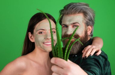 Eğlenceli çift için yüz yeşili maske. Aloe Vera ile yüz bakımı yapan komik bir çift. Güzellik uzmanı kadın ve erkeğin yüzünde yüz maskesi yapıyor. Kozmetik uzmanı aloe vera ile yüz prosedürü yapıyor