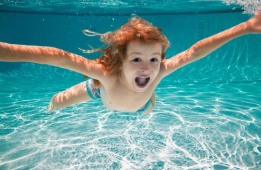 Heyecanlı çocuk havuzda su altında yüzüyor. Suyun altındaki çocuk. Çocuk yüzme ve havuzda yüzme ve suya dalma ile ilgili komik bir yüz resmi. Çocuklarla yaz eğlencesi. Aile yaz tatili