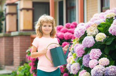 Bahçe işi. Bahar bahçıvanlığı. Bahçesinde sulama kutusu olan bir çocuk. Bitki ve bakım çiçekleri