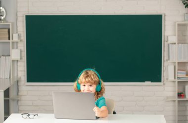 Kulaklıklı çocuk dizüstü bilgisayar kullanıyor ve okuldaki video öğretmeniyle internetten ders çalışıyor. İlkokul ve eğitim