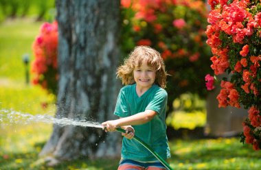 Çocuk, bir yaz akşamı evin arka bahçesindeki bahçede hortumla çiçekleri suluyordu.